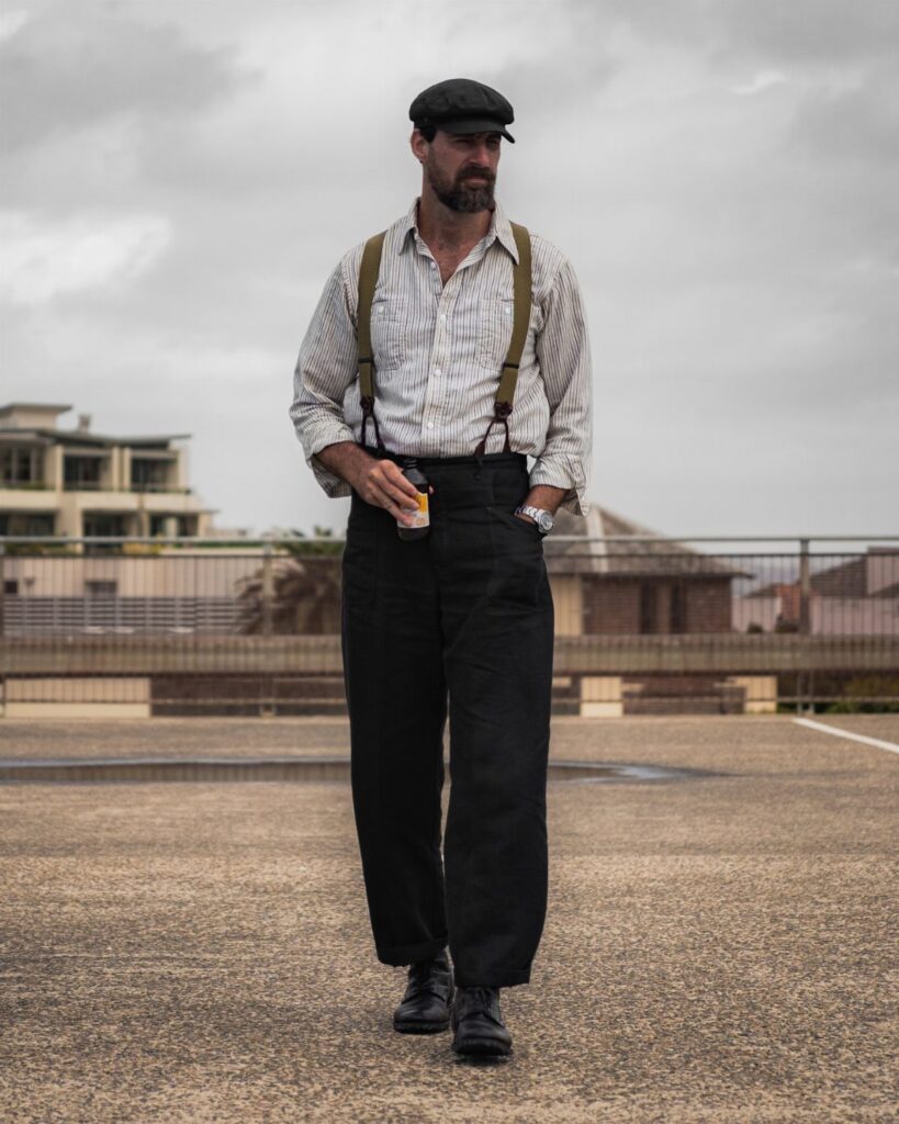 Man walking in vintage style clothing including a flat cap, striped shirt, and suspenders.