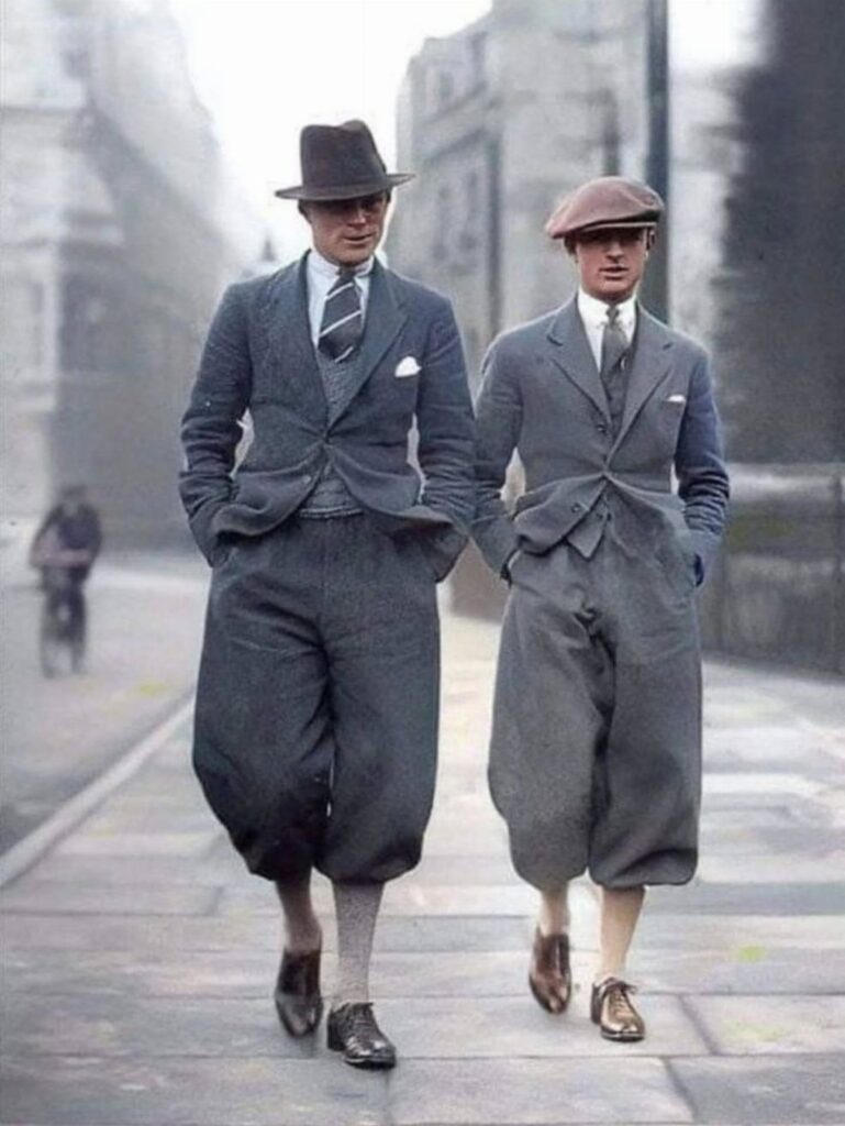 Two men walking in a city wearing vintage early 20th century suits and knickerbockers.