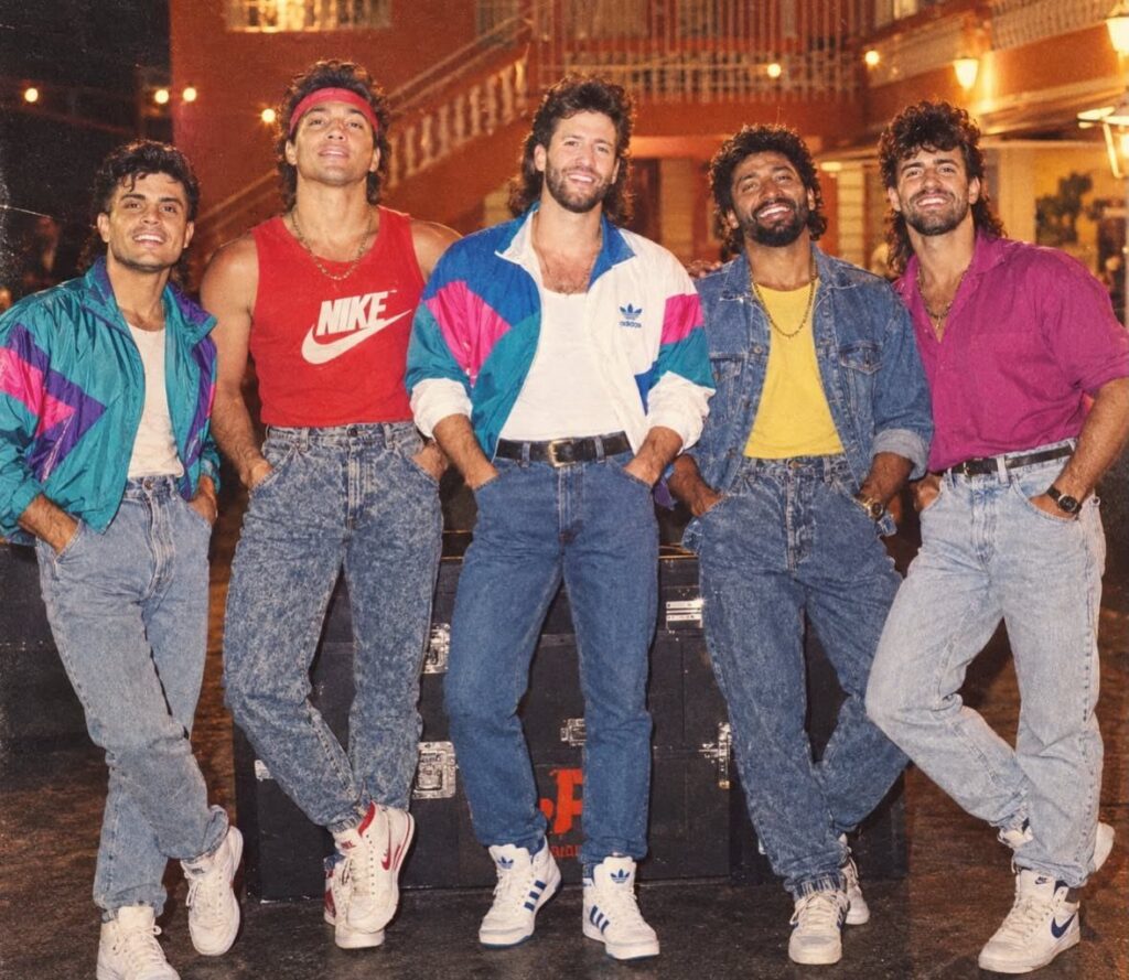 Five men posing in colorful 80s and 90s era fashion and denim jeans.