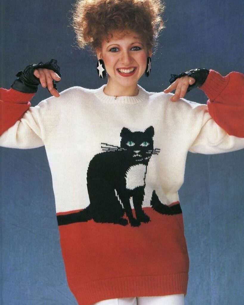 A woman smiling while wearing an oversized white and red sweater with a black cat graphic.