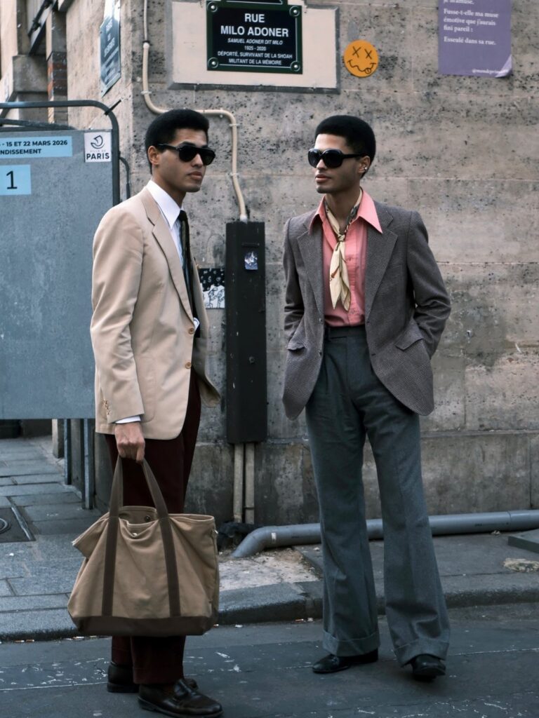 Two stylishly dressed men standing on a city street wearing blazers and trousers.