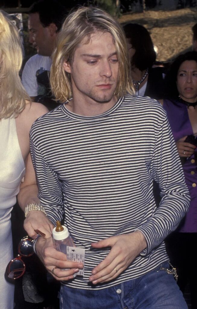 Kurt Cobain wearing a black and white striped long-sleeved shirt and blue jeans.