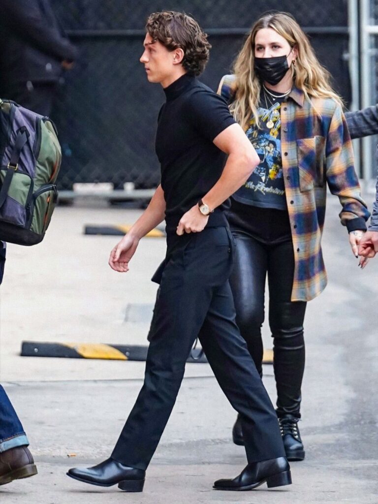 A man walking in black trousers and polished black leather boots.