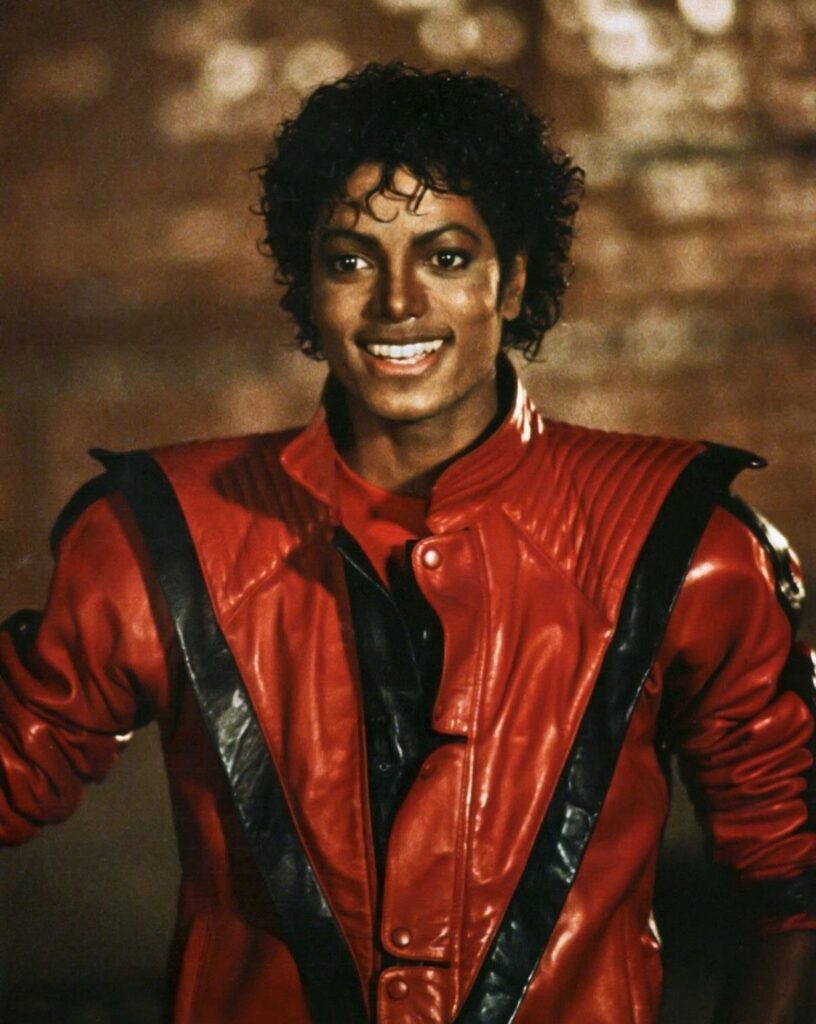 Michael Jackson smiling while wearing a distinctive red and black leather jacket.