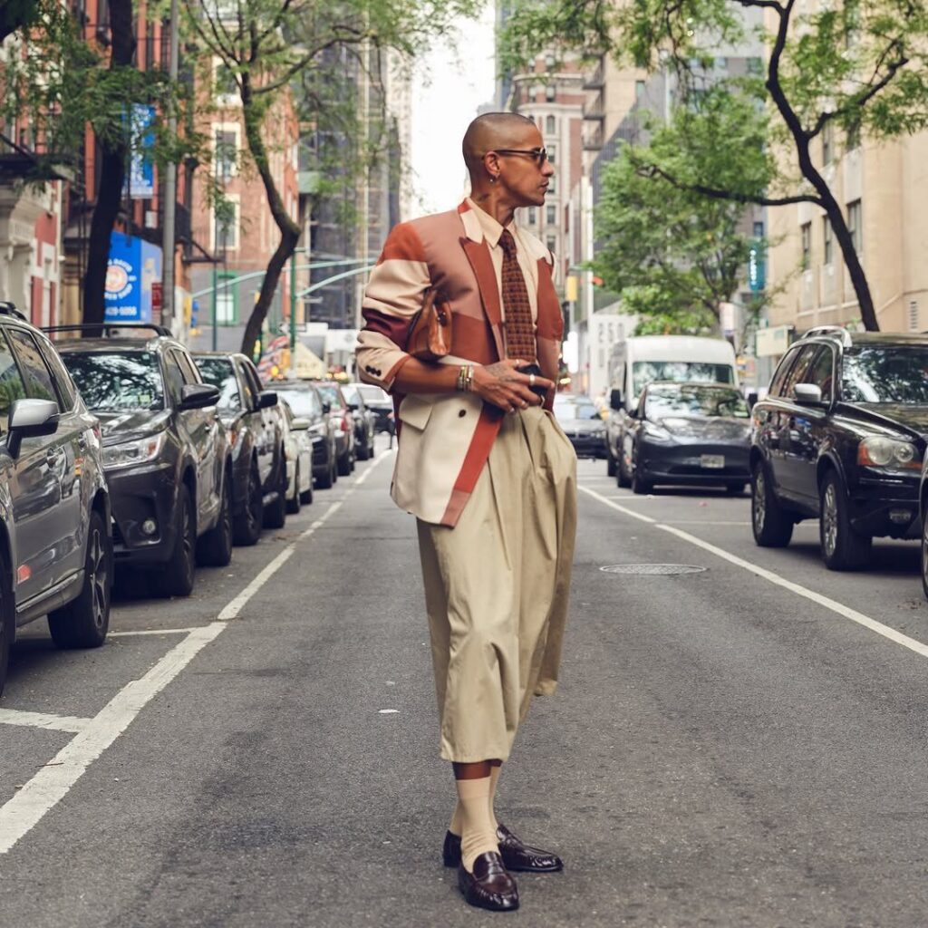 A stylish man in a patterned blazer and wide-leg trousers standing on a busy New York City street.