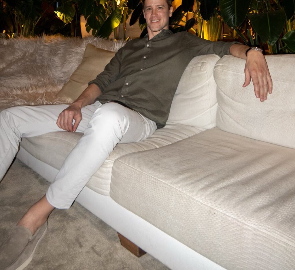 Man in olive shirt and white trousers relaxing on a white sofa.