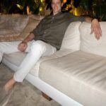 Man in olive shirt and white trousers relaxing on a white sofa.