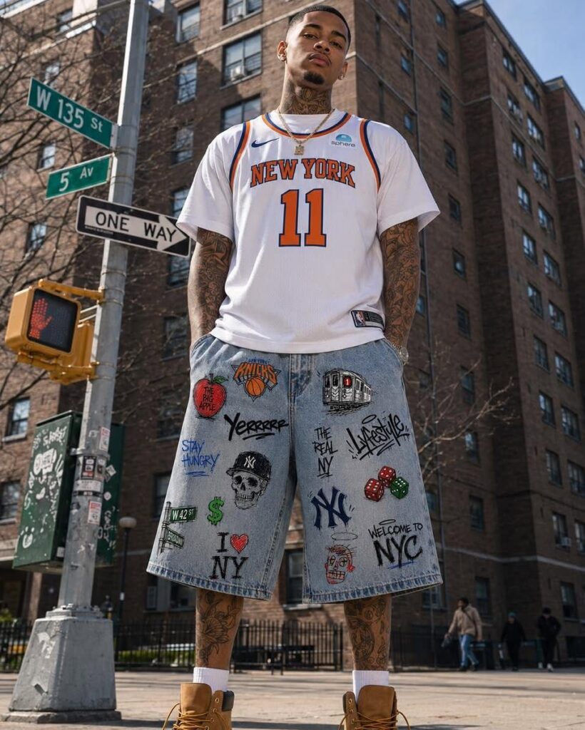 Man wearing a white New York jersey and graphic printed denim shorts standing on a city street.