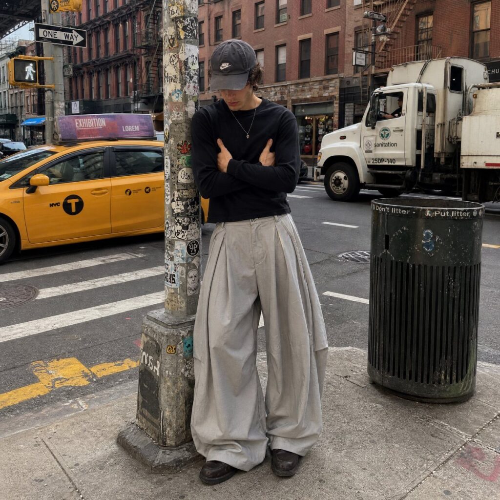 A person wearing voluminous light grey wide-leg trousers and a black shirt on a city street.