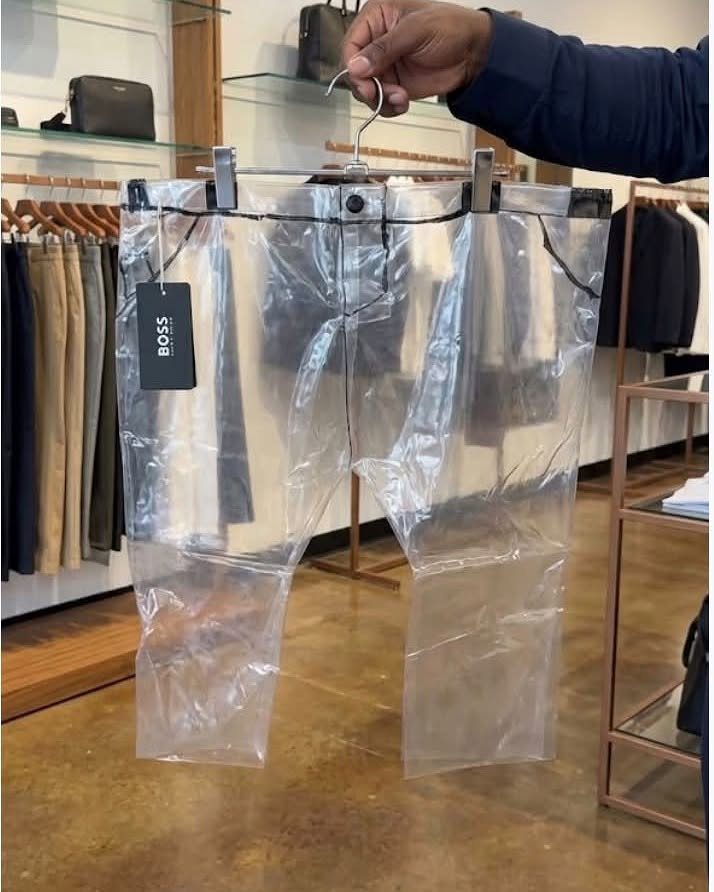 Transparent clear plastic trousers hanging on a metal hanger in a clothing store.